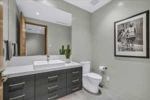 Modern powder room featuring a rectangular vessel sink, a light-toned countertop, a dark wood-finish vanity with ample storage, a large wall-mounted mirror, and tile flooring
