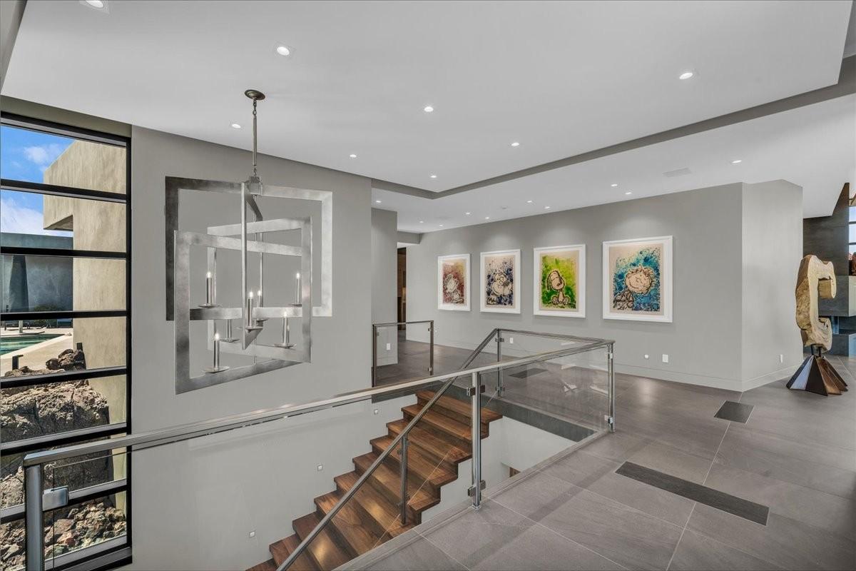 Contemporary staircase featuring wood-finish treads, glass railings with metal handrails, and a modern chandelier
