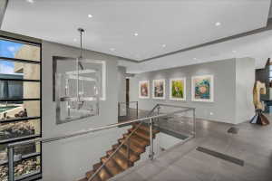 Contemporary staircase featuring wood-finish treads, glass railings with metal handrails, and a modern chandelier
