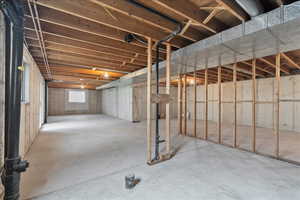 Expansive unfinished basement featuring concrete flooring, exposed ceiling joists, wood framing, a window, and exposed ductwork