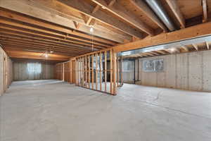 Expansive unfinished basement featuring concrete flooring and exposed ceiling joists