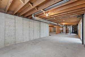 Spacious unfinished basement featuring exposed wood joists, concrete walls, concrete flooring, and visible ductwork