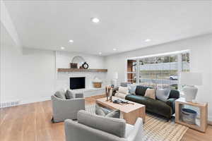 Living area featuring a white brick fireplace with a wood mantle, recessed lighting, and wood-finish flooring