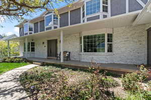 Traditional-style exterior featuring a covered front porch with white columns, light-colored brick siding, and bay windows with grid patterns