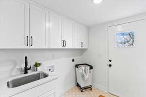 Laundry area featuring white shaker cabinetry with black hardware, a stainless steel sink with a matte black faucet, and a light-toned patterned floor