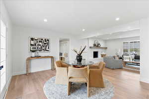 Open-concept living space featuring light wood-finish flooring, recessed lighting, and a white brick fireplace with a wood-beam mantel