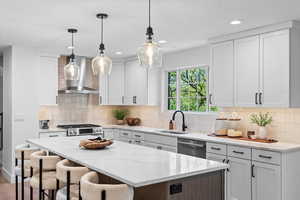 Kitchen featuring a large central island with seating, white shaker cabinetry, stainless steel appliances, and elegant pendant lighting