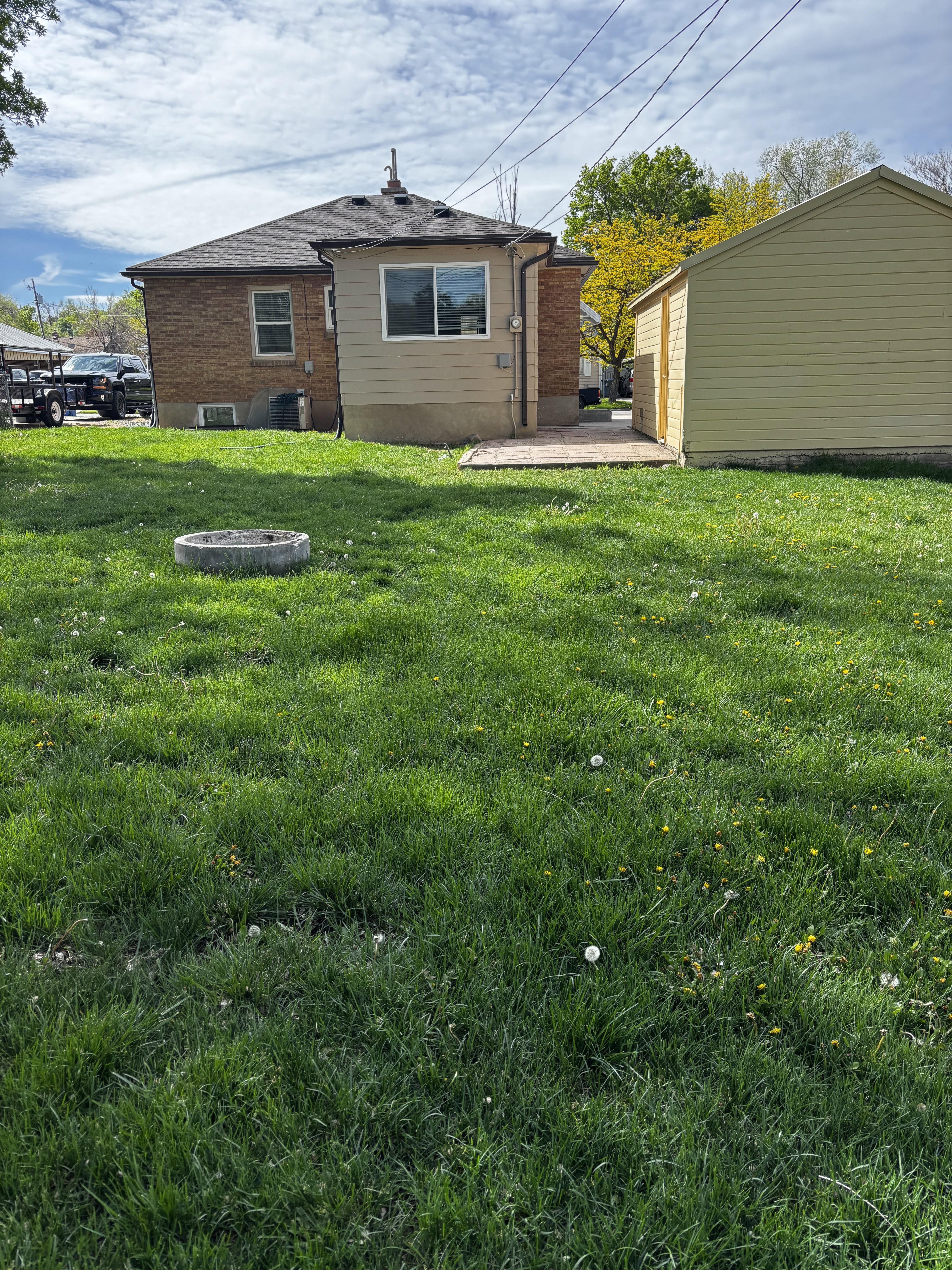Spacious backyard featuring a detached accessory structure, a small elevated deck, and a brick exterior with a siding addition