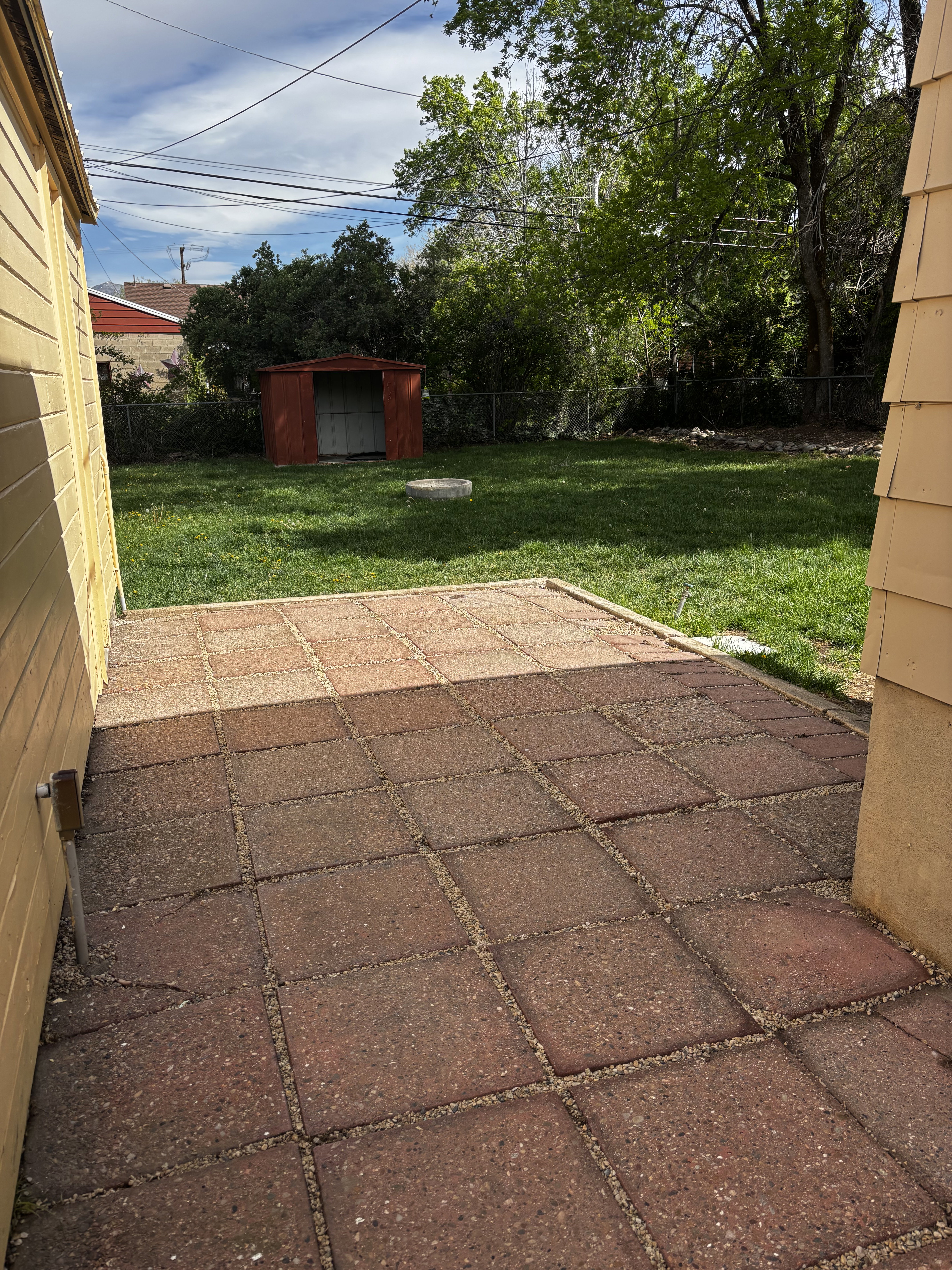 Expansive backyard featuring a red paver patio, established lawn, mature trees, and a metal storage shed