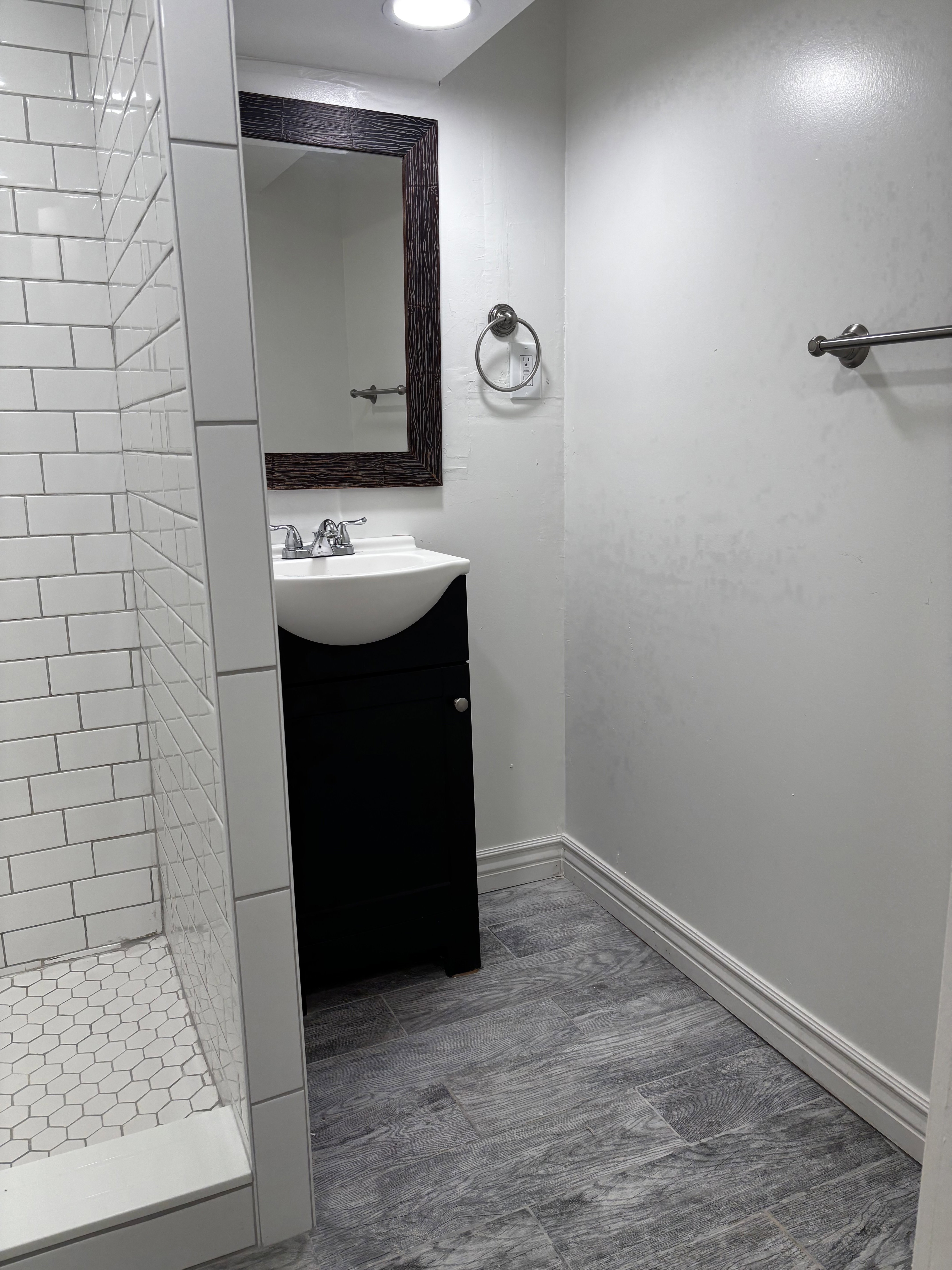 Bathroom featuring a black vanity with an integrated white sink, a framed mirror, and a white subway tile shower with a hexagonal tile floor