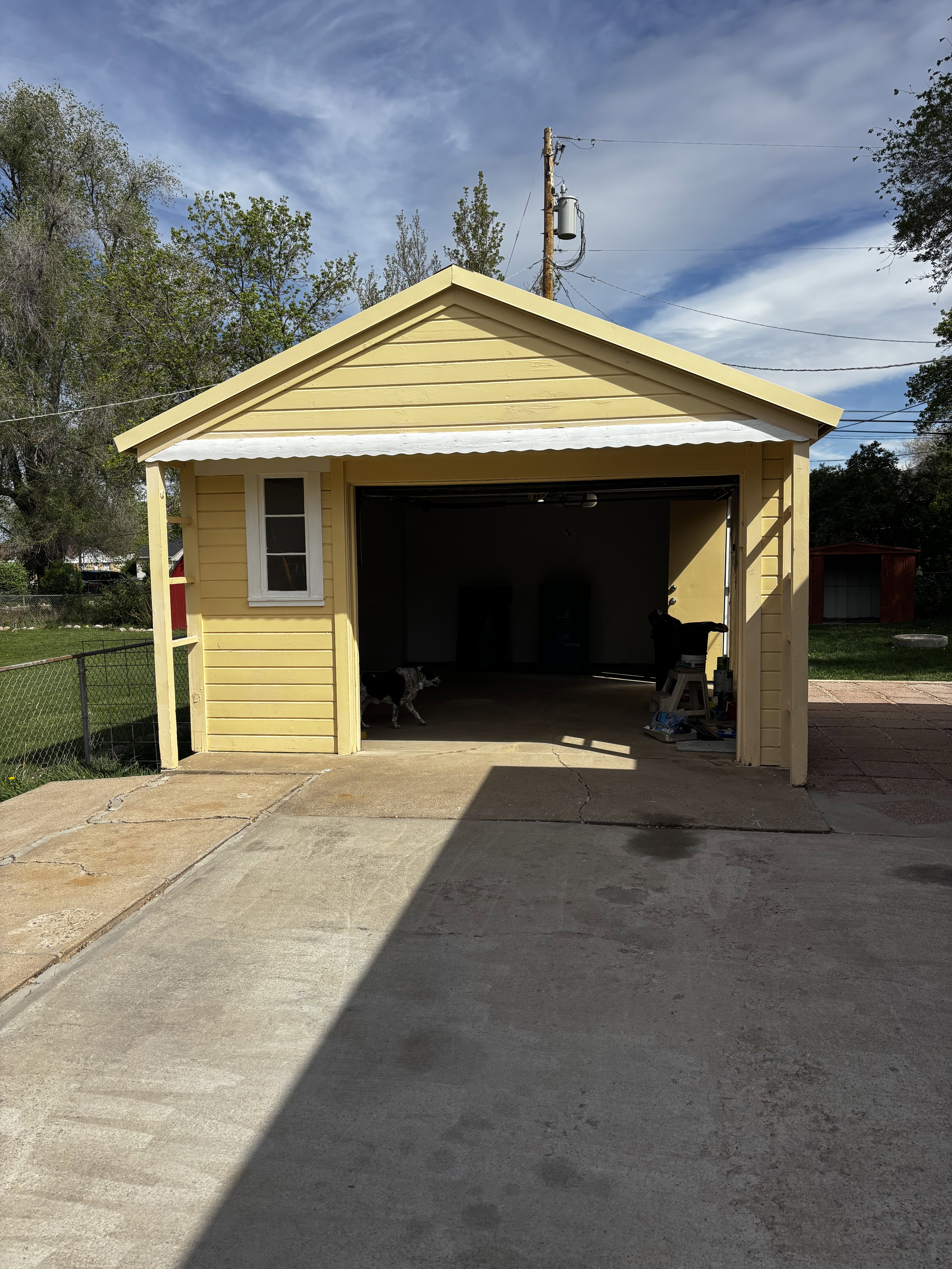 Detached garage featuring yellow siding, a white window, and a corrugated metal awning