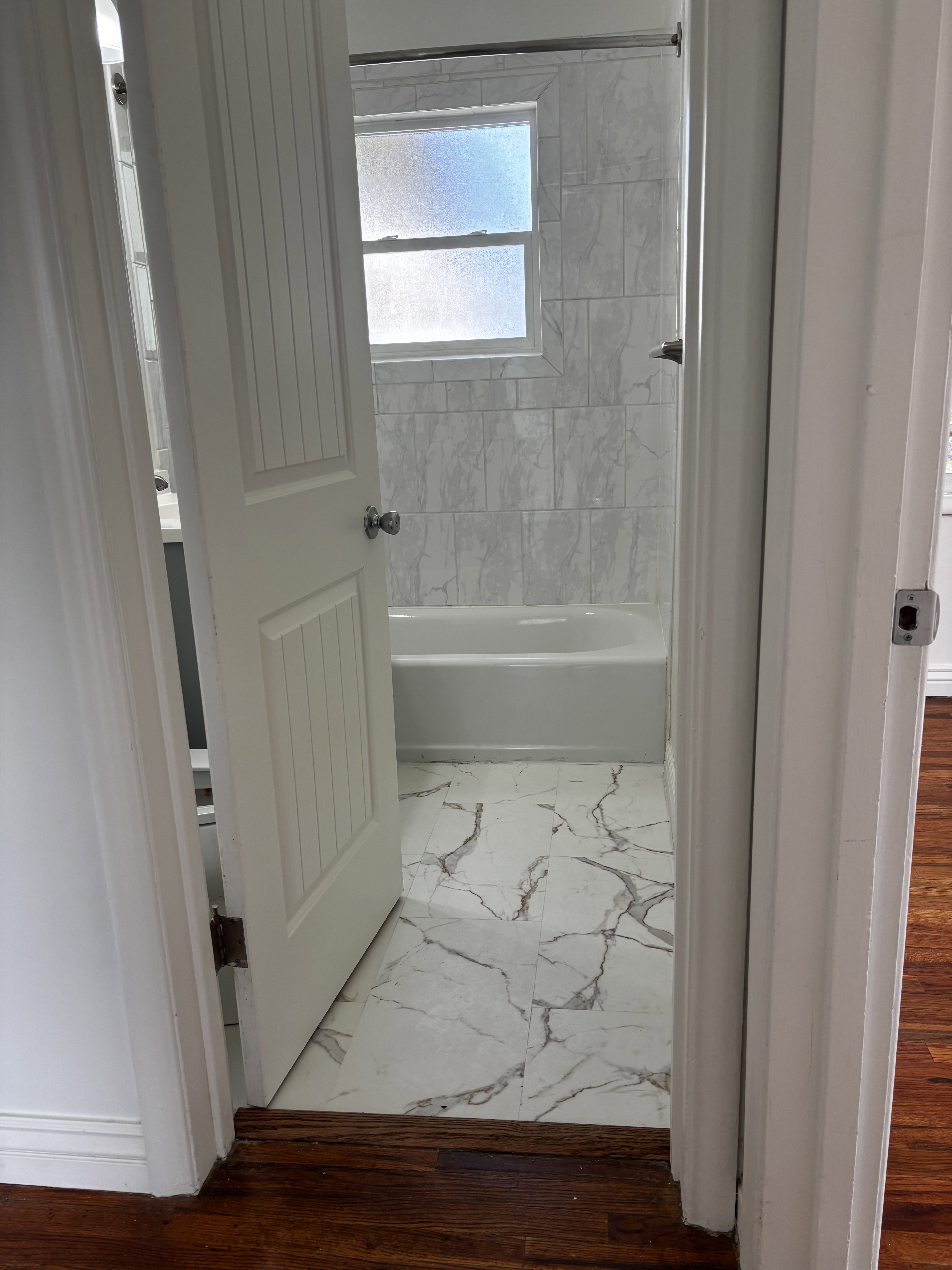 Bathroom featuring a white bathtub, grey subway tile shower surround, and a window with frosted glass