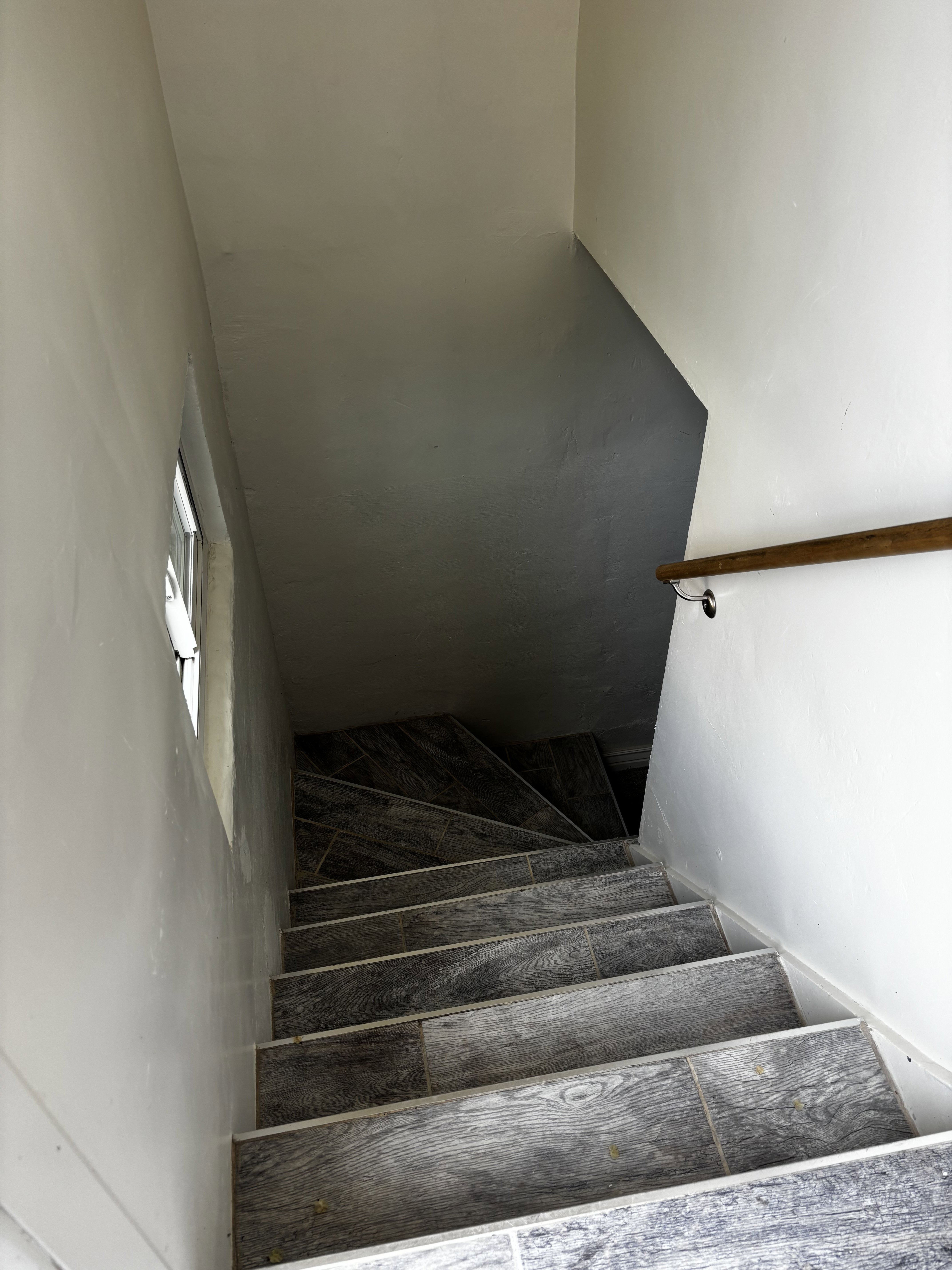 Staircase featuring wood-look tile treads and risers, a natural wood handrail, and a small window for ambient light