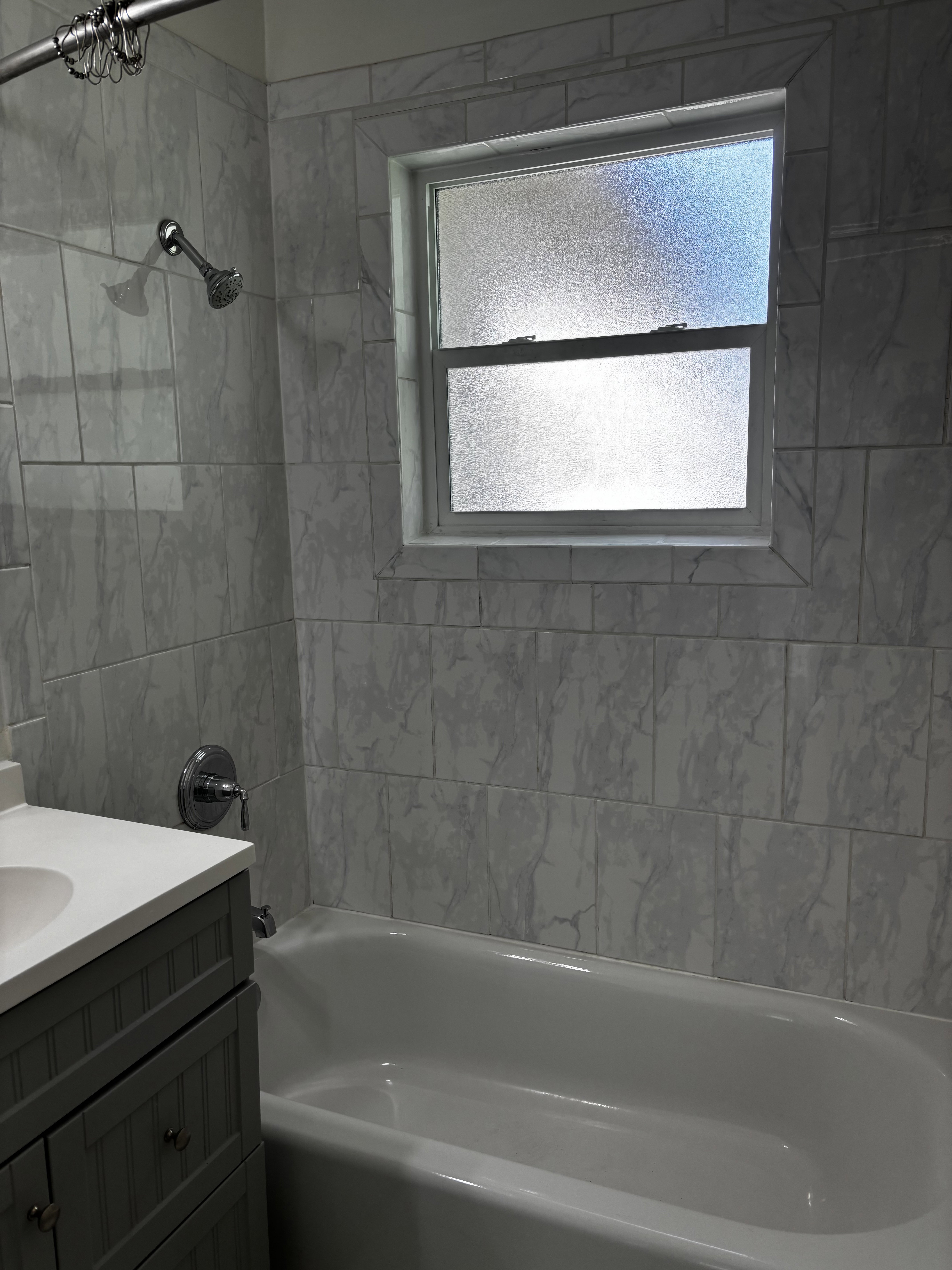 Bathroom featuring a white bathtub, light-toned tile surround, and a frosted window