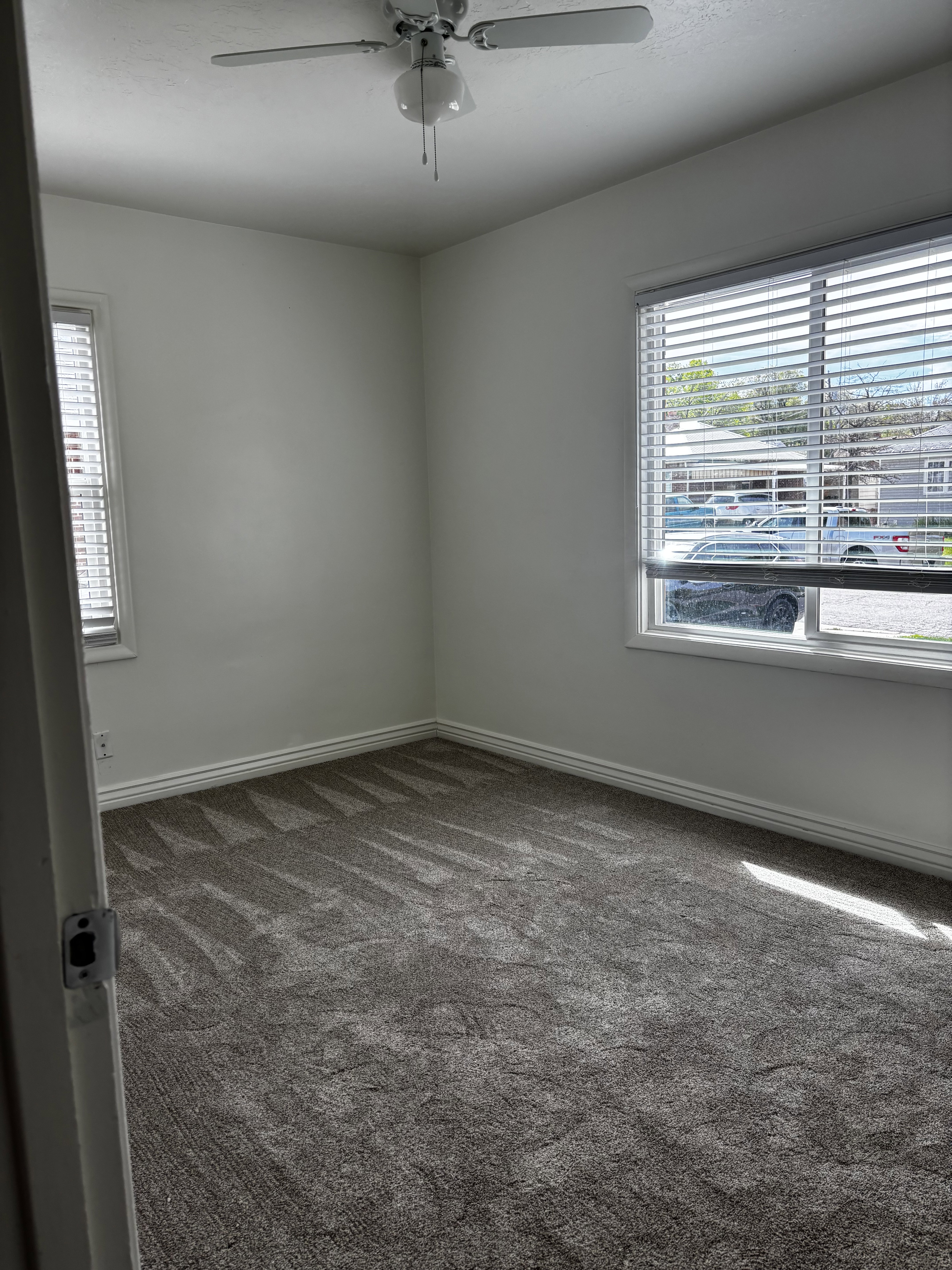 Room featuring plush gray carpet, white walls, and a ceiling fan with integrated lighting