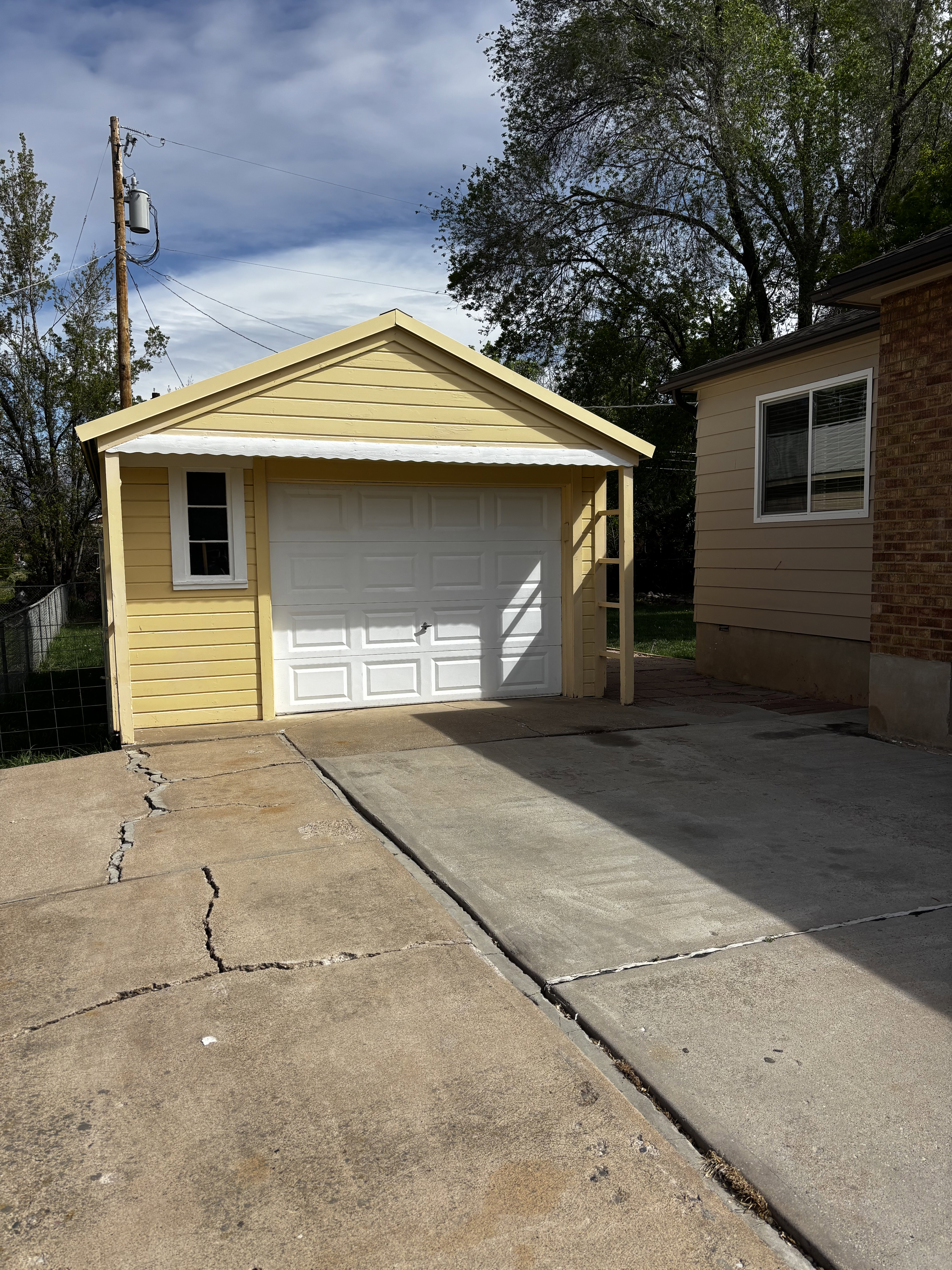Detached single-car garage with a white panel door and a side window, featuring yellow siding and a gabled roofline