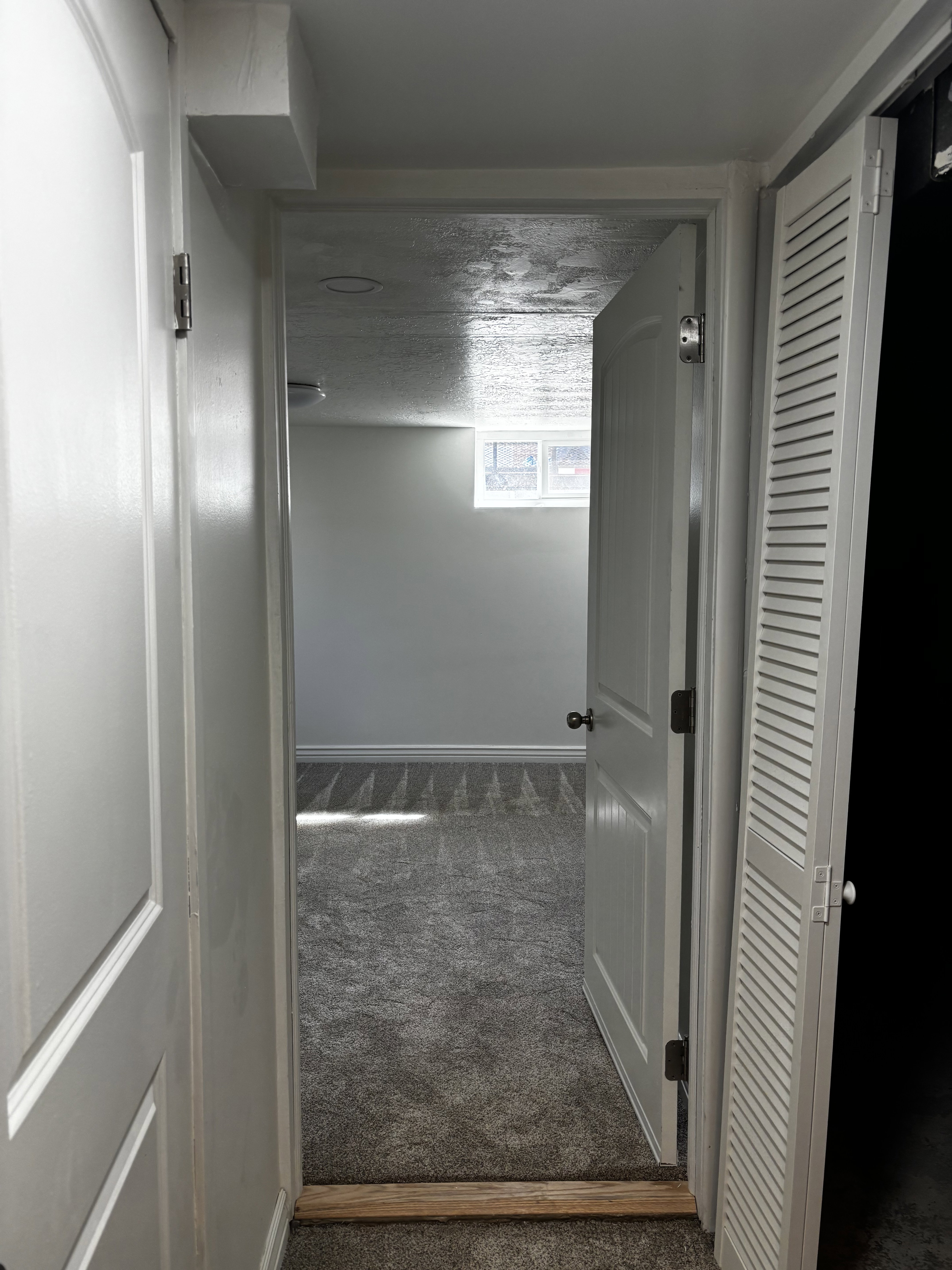 Interior space featuring gray carpet flooring, white painted walls, and a window providing natural light