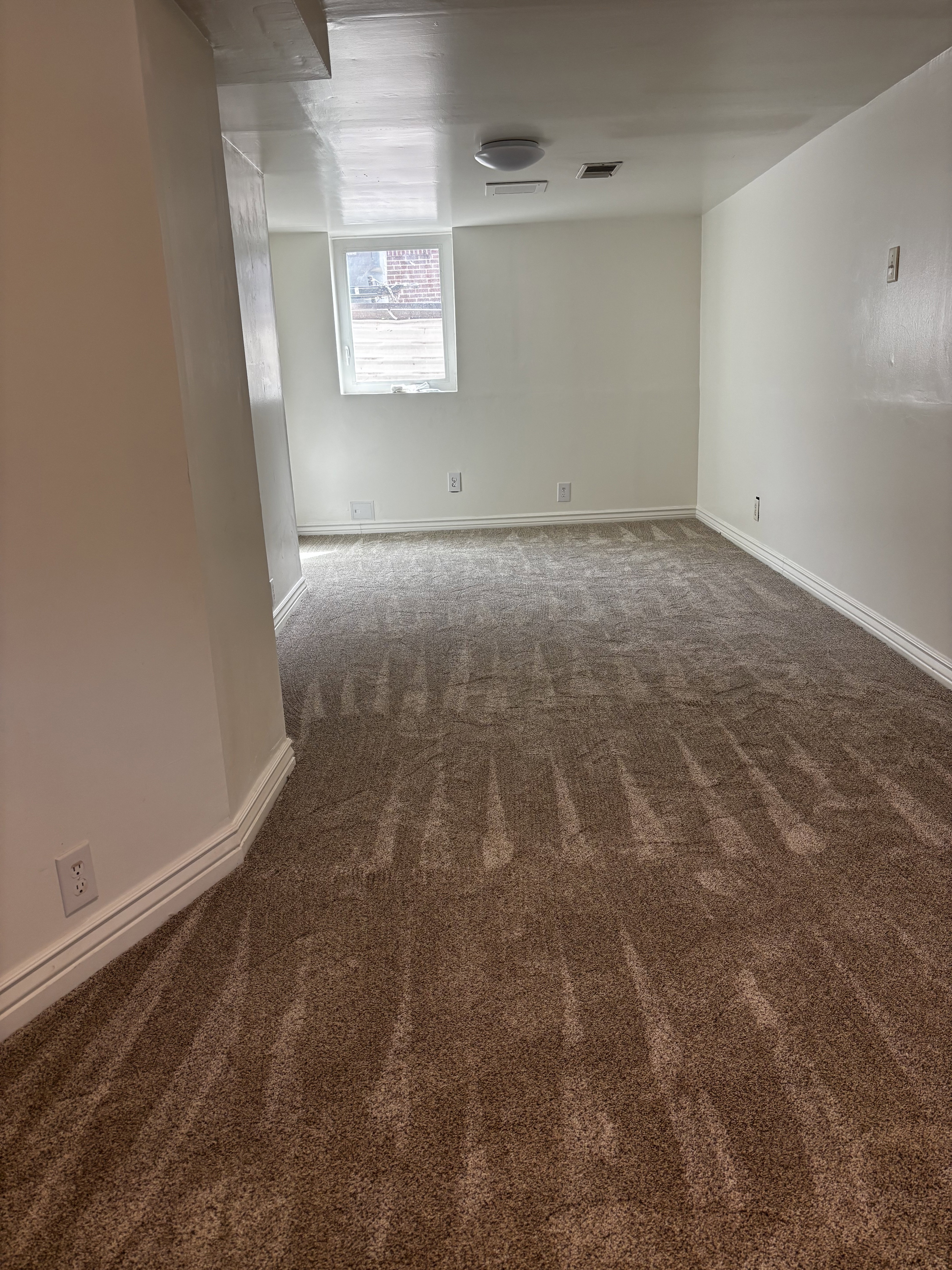 Spacious room featuring new brown carpet, white baseboards, and a single window