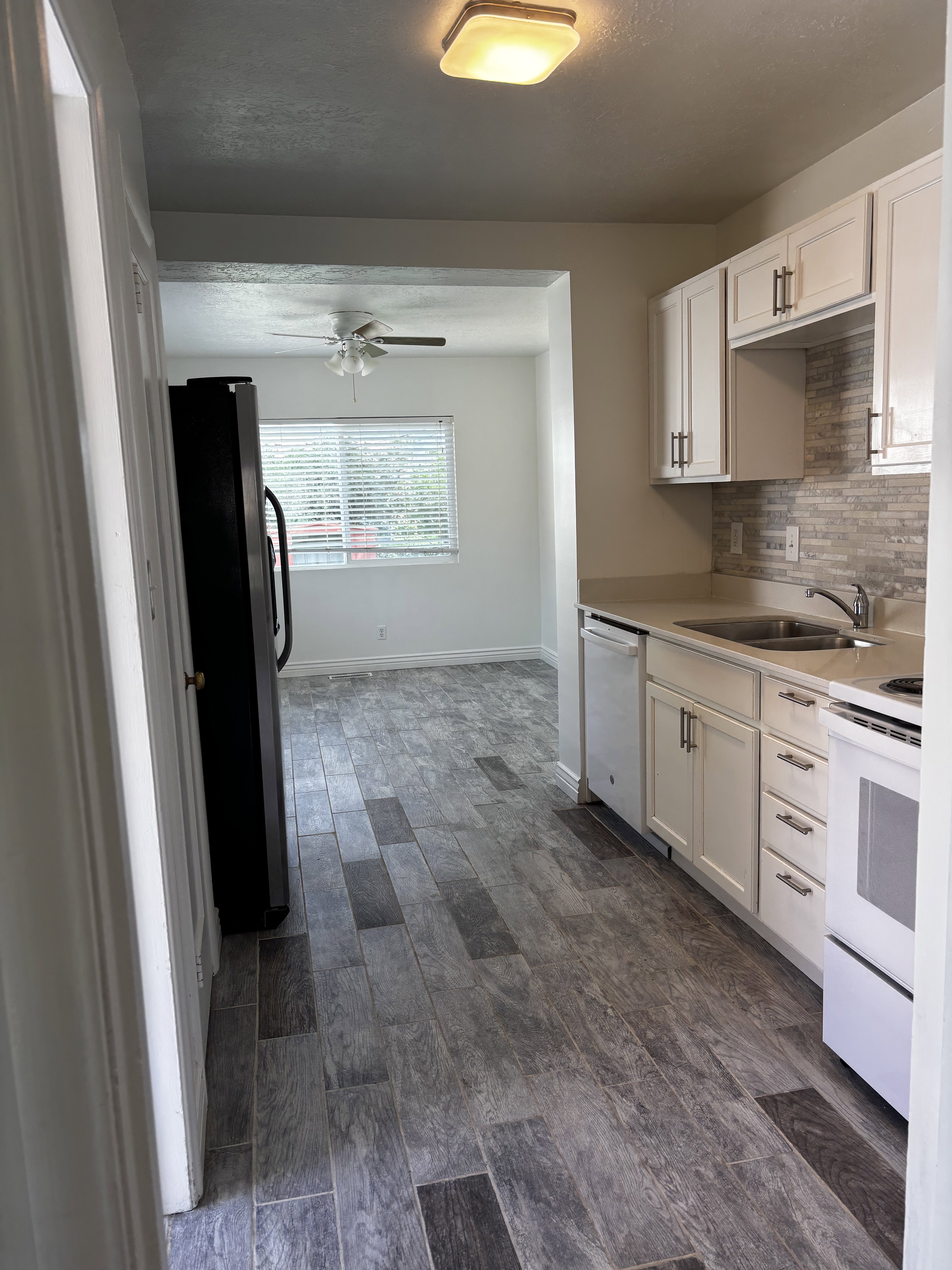 Kitchen featuring wood-finish flooring, white cabinetry, a light-toned backsplash, and a double-basin sink