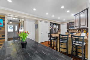 Open-concept living space featuring recessed lighting, crown molding, a kitchen peninsula  with granite countertops, a tile backsplash, and hardwood flooring