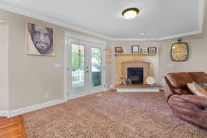 Living space featuring a corner fireplace with a brick surround and wood mantel, white crown molding, and double glass-paneled doors opening to an outdoor area