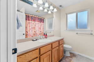 Full guest bathroom featuring a light-toned countertop, wood-finish cabinetry, an integrated sink with chrome faucet, and a toilet