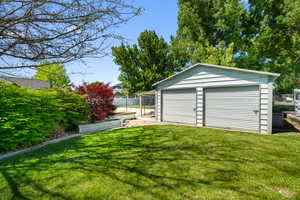 Expansive green lawn with a two-car shop featuring roll-up doors, surrounded by mature trees and shrubs