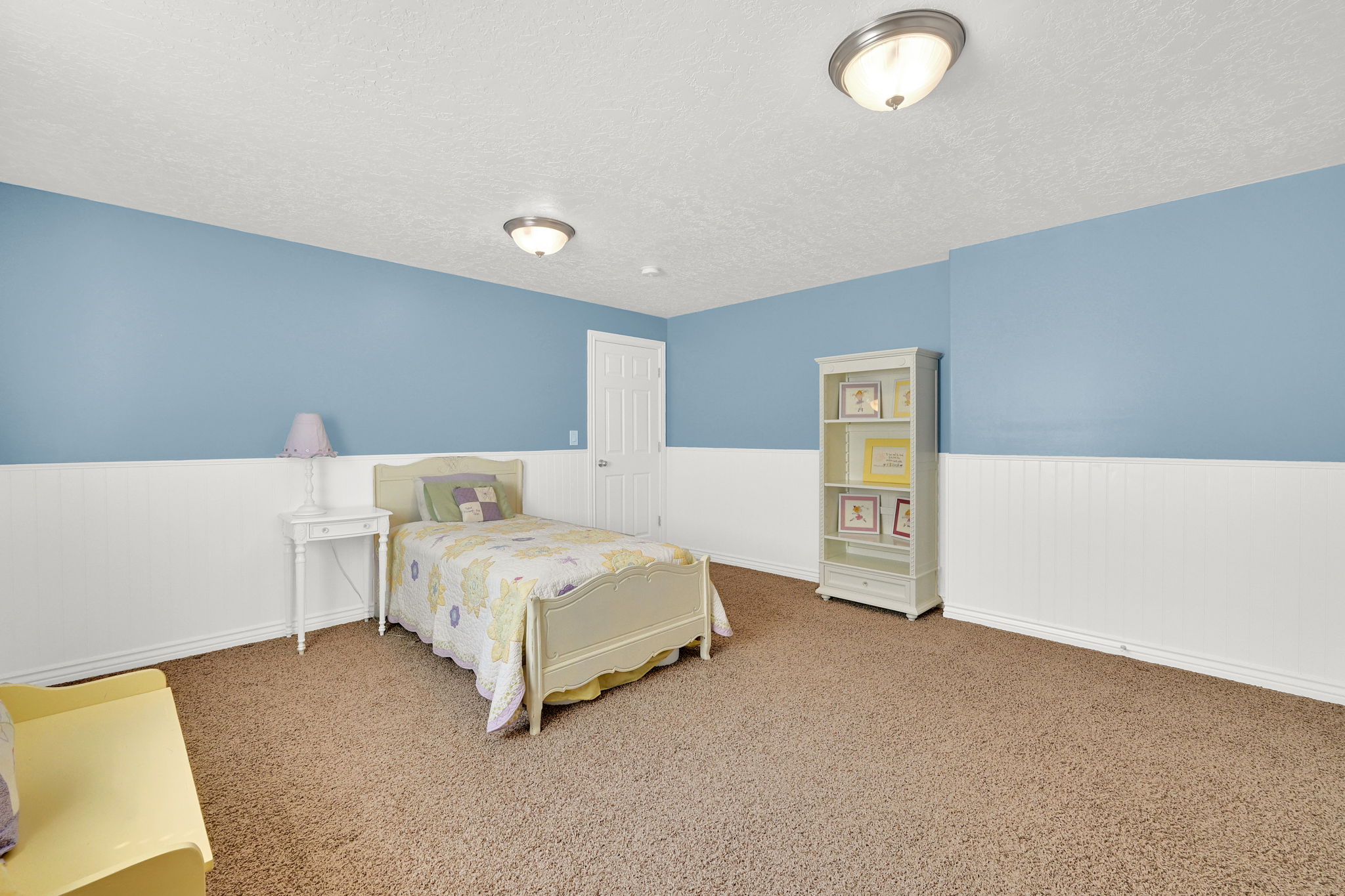 Spacious room featuring light blue walls with white wainscoting, brown carpet flooring, and white trim