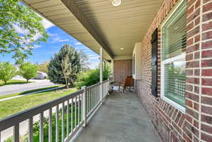 Covered front porch featuring a concrete surface, white railings, and a brick exterior