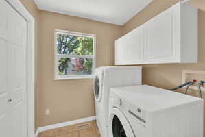 Laundry area featuring a window, white cabinetry, a bi-fold door, and tile flooring