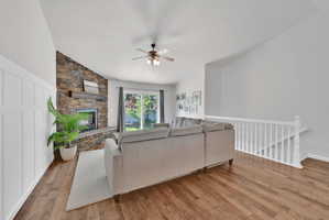 Living area featuring wood-finish flooring, a stone-clad fireplace with a dark wood mantel, board and batten accent wall, and vaulted ceilings