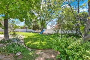 Spacious backyard featuring a manicured lawn, established landscaping, mature trees, and a white perimeter fence