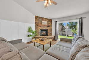 Living area featuring a stone-clad fireplace with a wood mantle, vaulted ceiling, and wood-finish flooring
