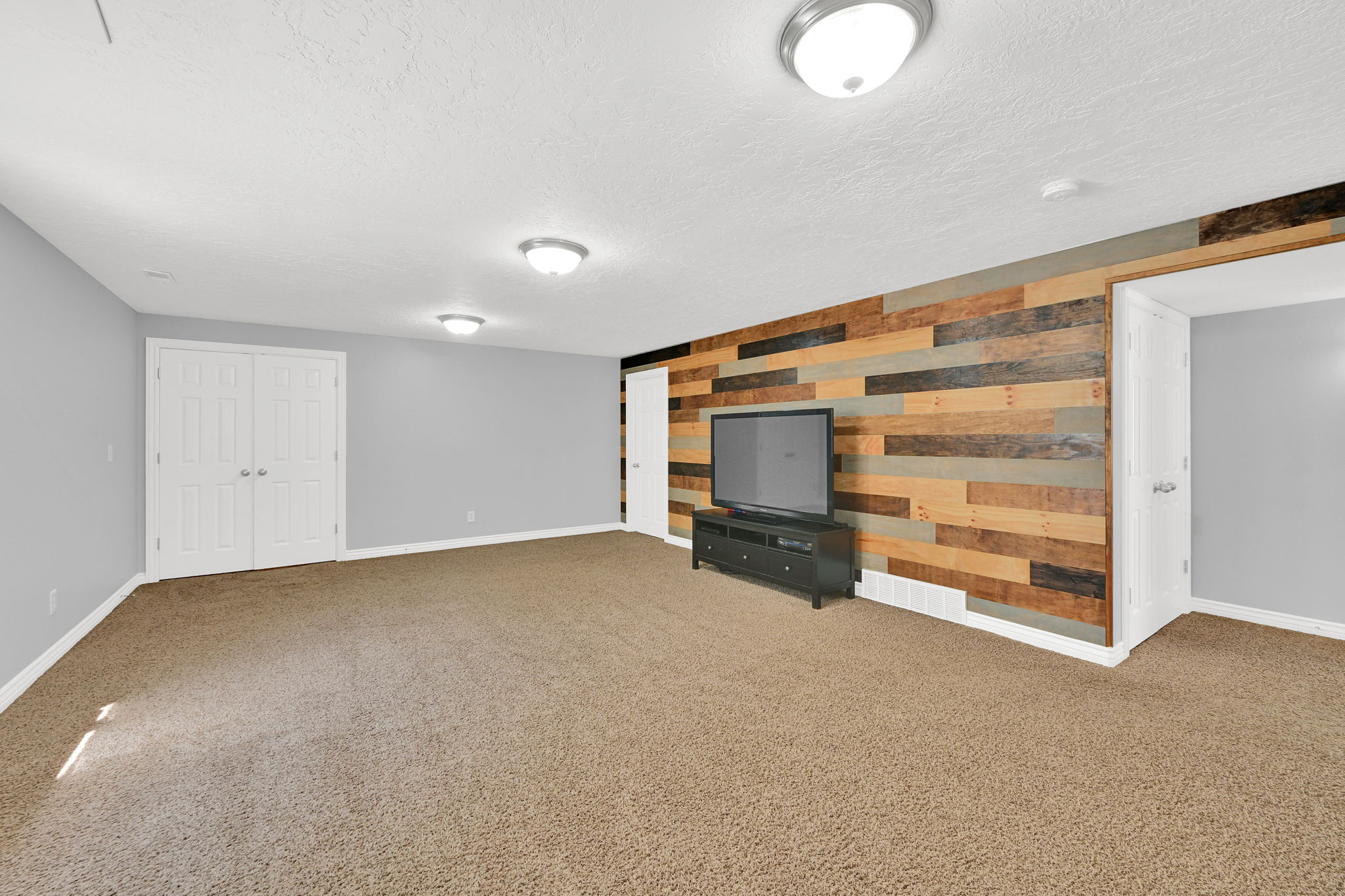 Spacious room featuring a multi-toned wood plank accent wall, neutral carpeting, and light gray painted walls