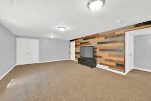 Spacious room featuring a multi-toned wood plank accent wall, neutral carpeting, and light gray painted walls