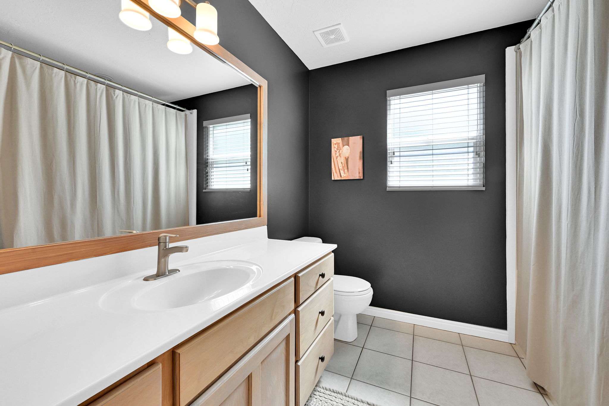 Bathroom featuring a wood-finish vanity with a white countertop and integrated sink, brushed nickel faucet, and tile flooring