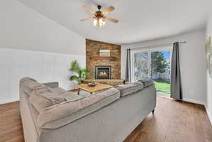Living area featuring vaulted ceilings, wood-finish flooring, and a stone-clad fireplace with a wood mantel