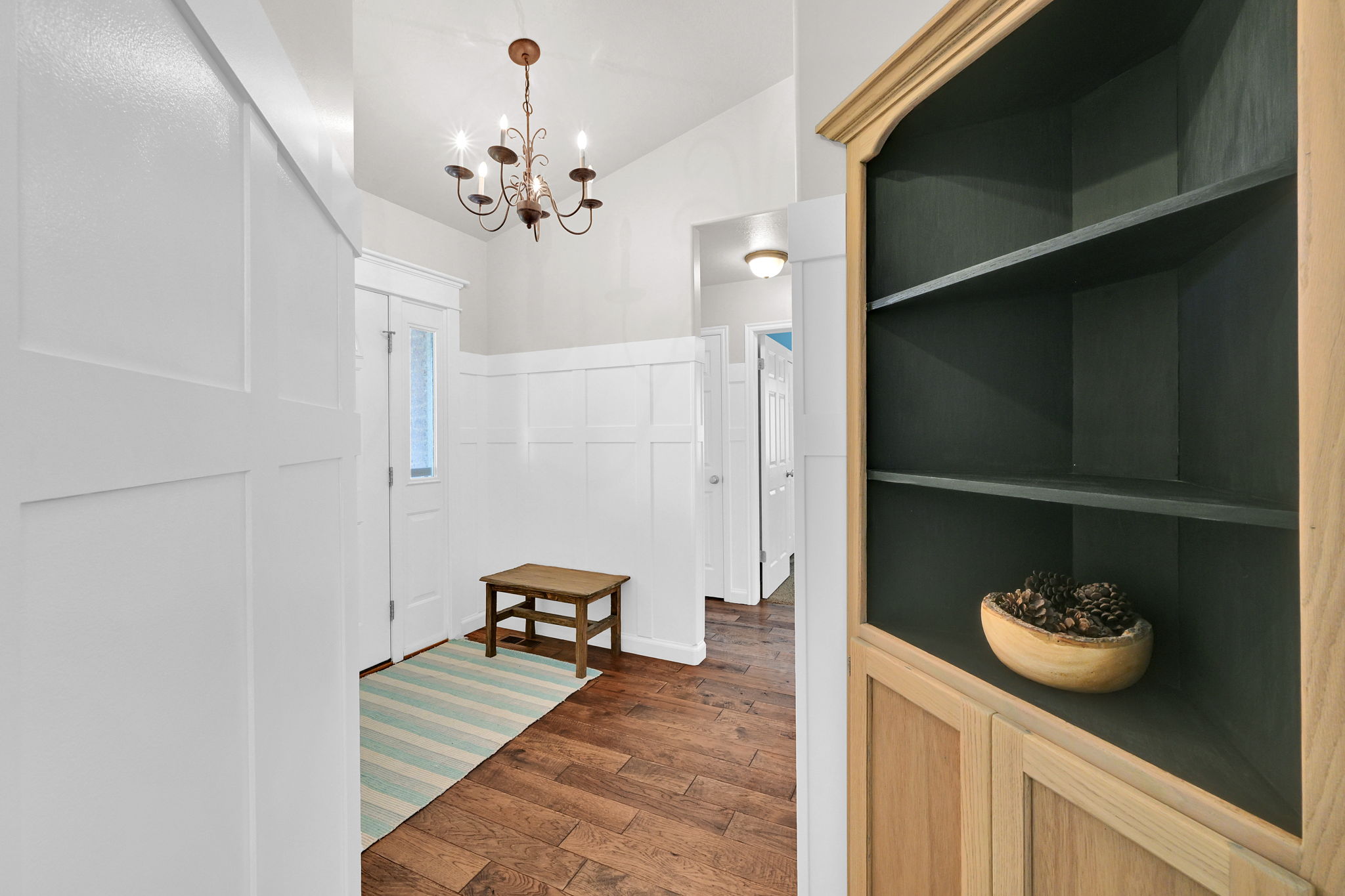 Entryway featuring wood-finish flooring, white wainscoting, and an overhead chandelier