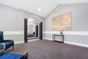 Spacious room featuring vaulted ceilings, textured carpeting, and wainscoting