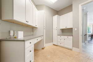 Workstation featuring extensive white cabinetry, a built-in desk, and light-toned tile flooring