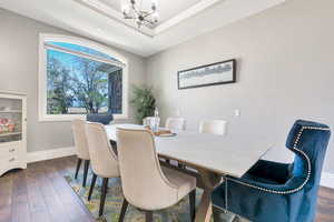 Dining area featuring an arched window, wood-finish flooring, a tray ceiling with a chandelier, and a built-in display cabinet