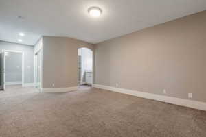 Spacious carpeted room featuring a neutral color palette, recessed lighting, and an arched entry to an en-suite area with a vanity
