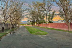 Asphalt driveway with a central grassy median, bordered by mature trees and a combination of stone and red brick perimeter walls