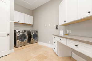 Dedicated laundry space featuring stone-finish flooring, white shaker-style cabinetry with matte black hardware, a light-toned countertop, and built-in front-loading appliances