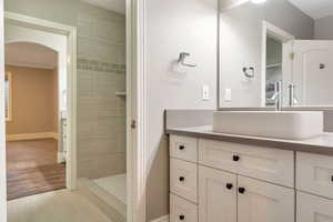 Bathroom featuring a vessel sink, a vanity with shaker-style cabinetry and dark hardware, a large mirror, and a walk-in shower with tiled walls and a decorative accent band