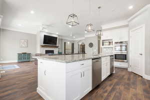 Open-concept kitchen featuring a large island with a stone countertop, white shaker cabinetry, stainless steel appliances, and wood-finish flooring