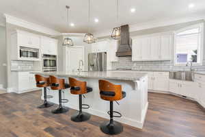 Spacious kitchen featuring an expansive center island with seating, stainless steel appliances, white cabinetry, wood-finish flooring, and a farmhouse sink