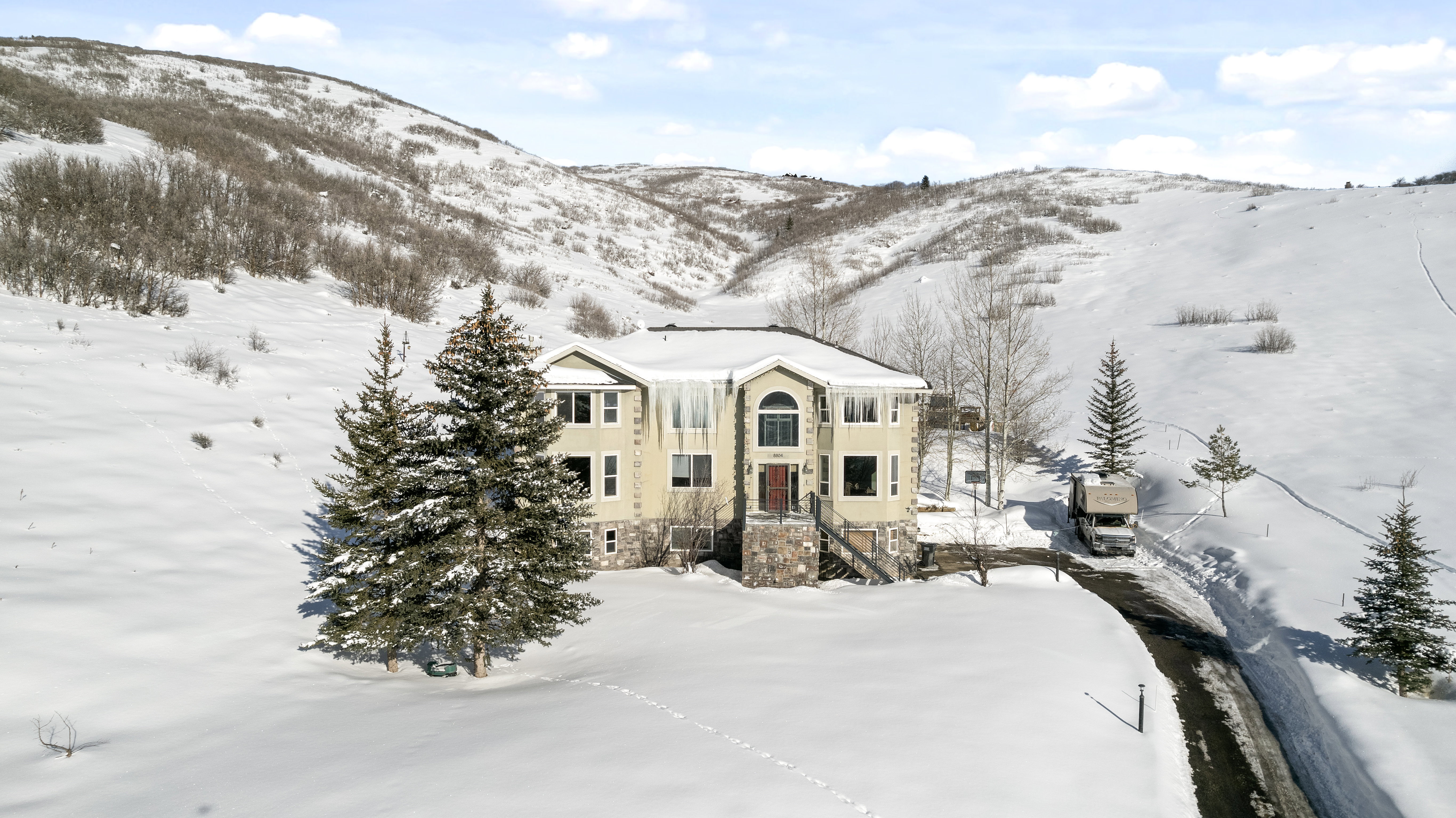Contemporary multi-level residence featuring a neutral-toned exterior, stone accents, and a dark asphalt driveway