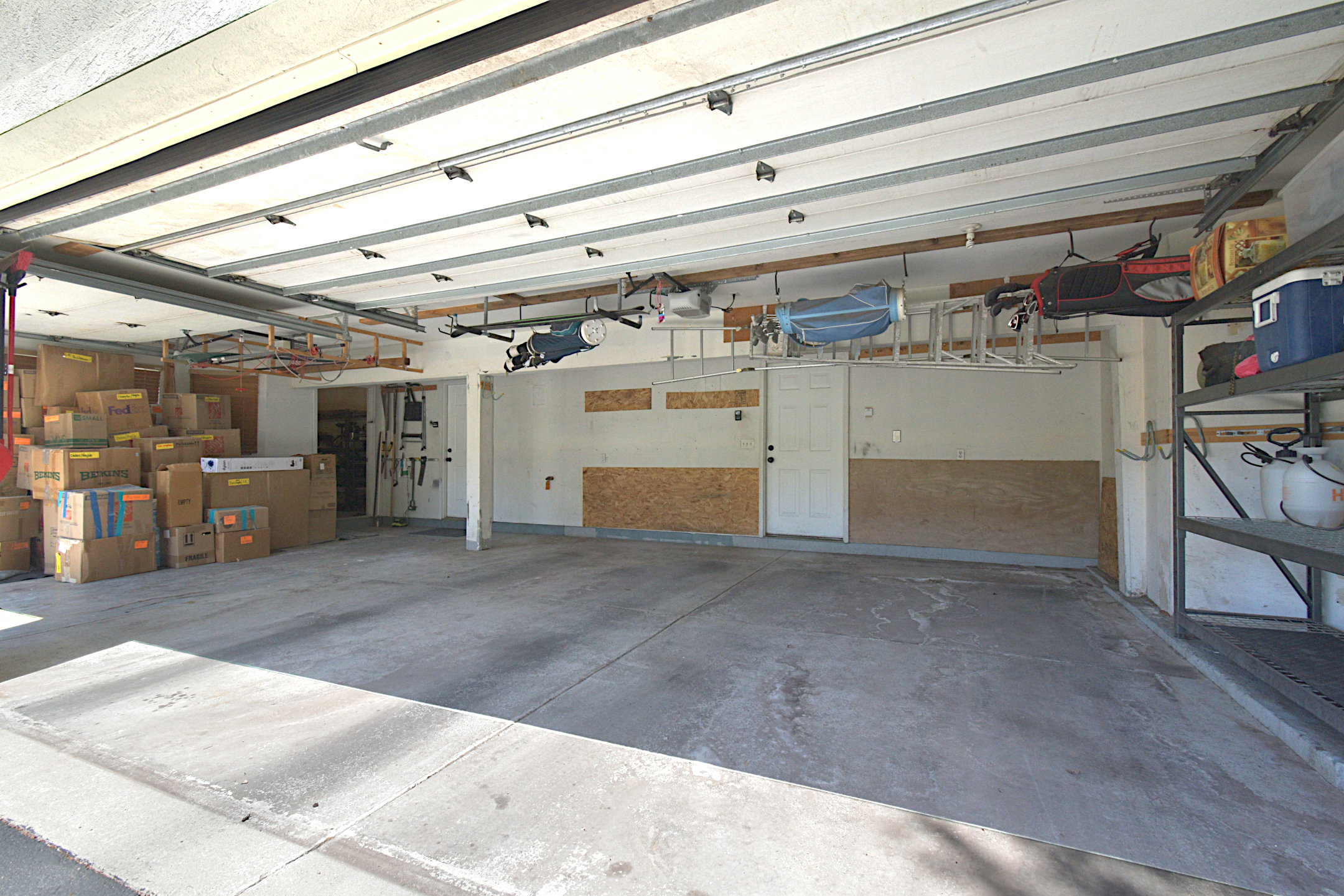 Spacious garage featuring a concrete floor, built-in shelving, overhead storage racks, a side entry door, and a partially finished wall