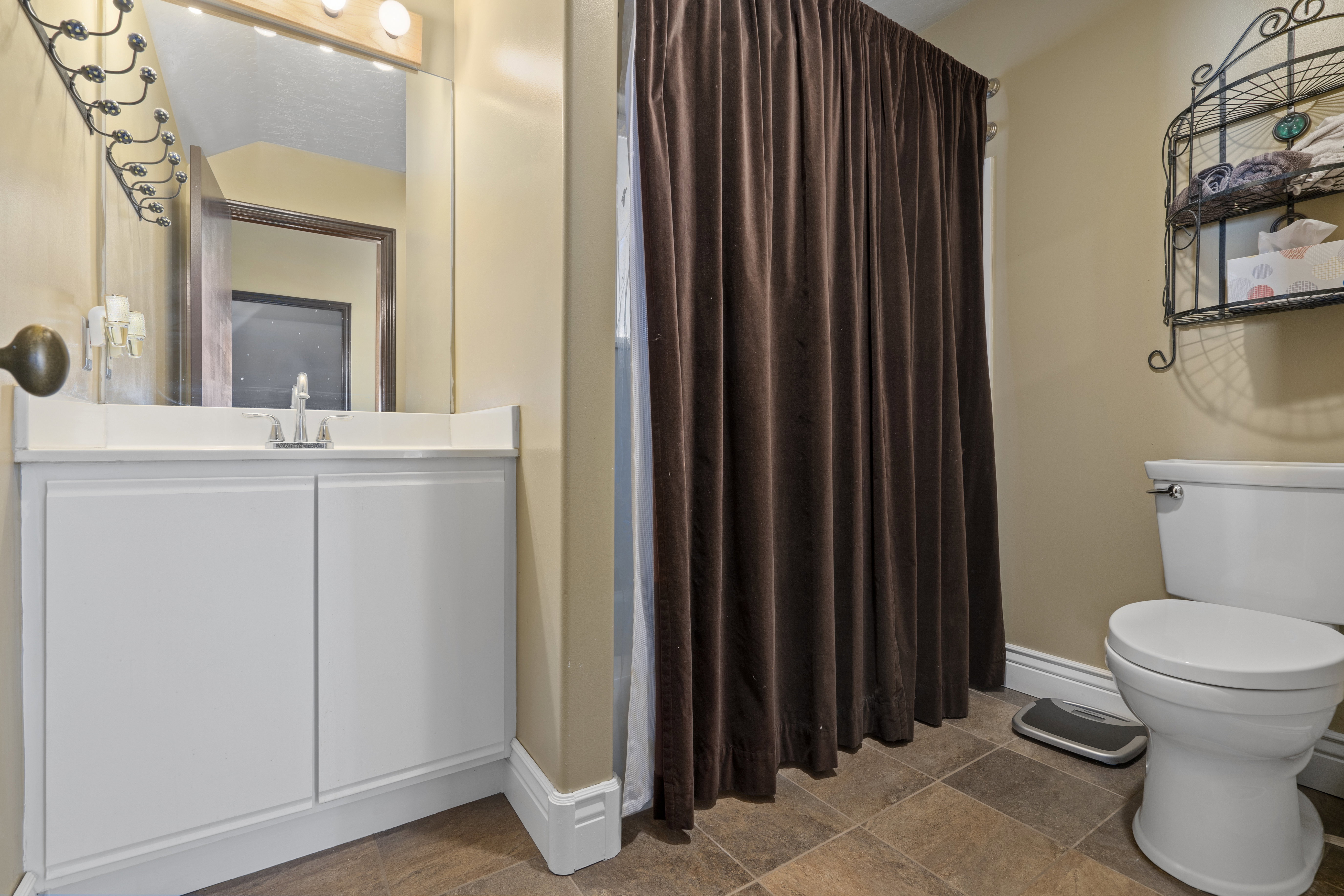 Bathroom featuring a white vanity with an integrated sink, a wall-mounted mirror, and a shower area with a brown curtain